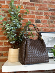 Dark brown vegan leather woven shoulder bag with braided straps and gold hardware. 