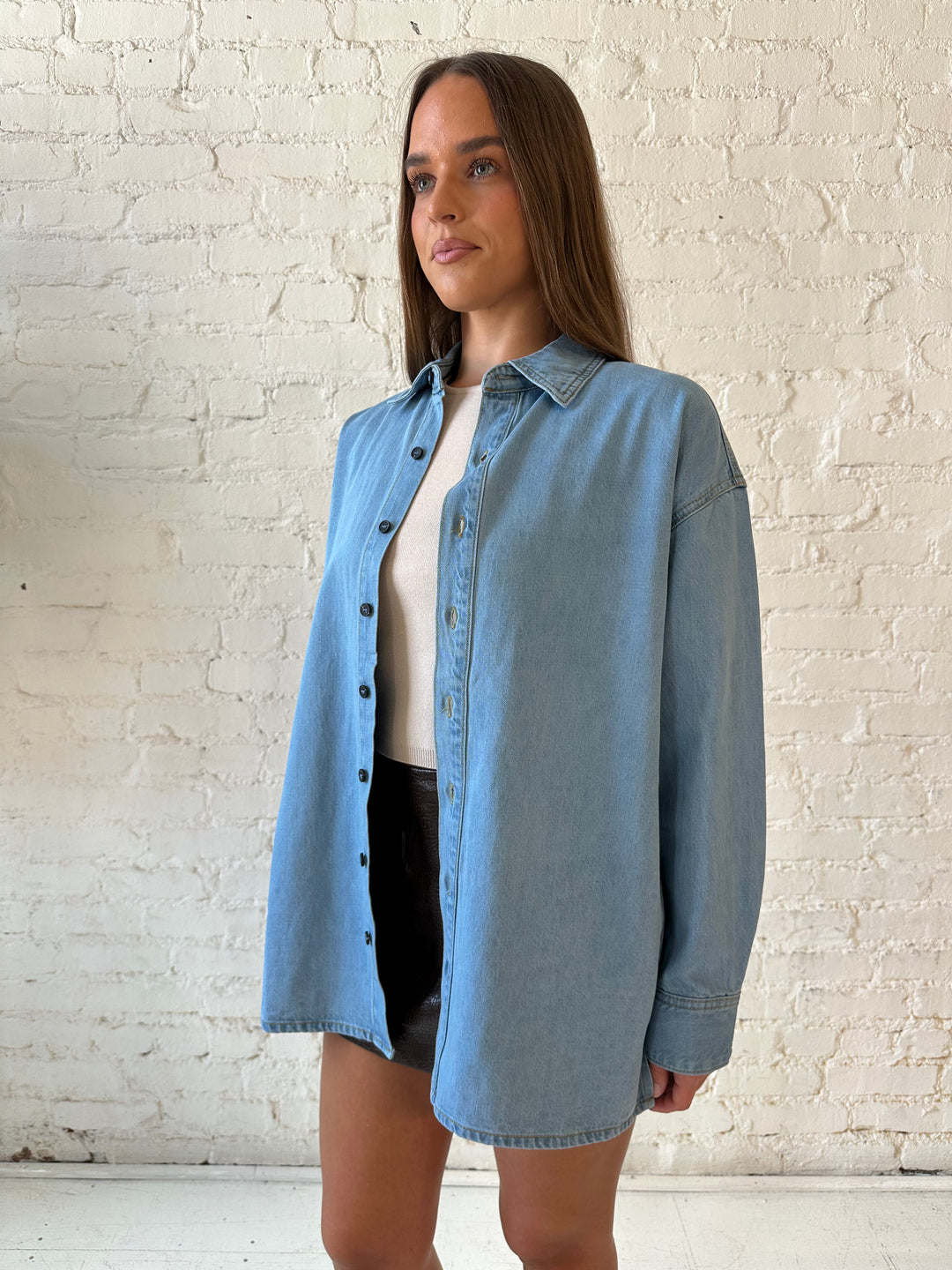 Woman wearing light wash button down denim shirt with leather mini skort. 