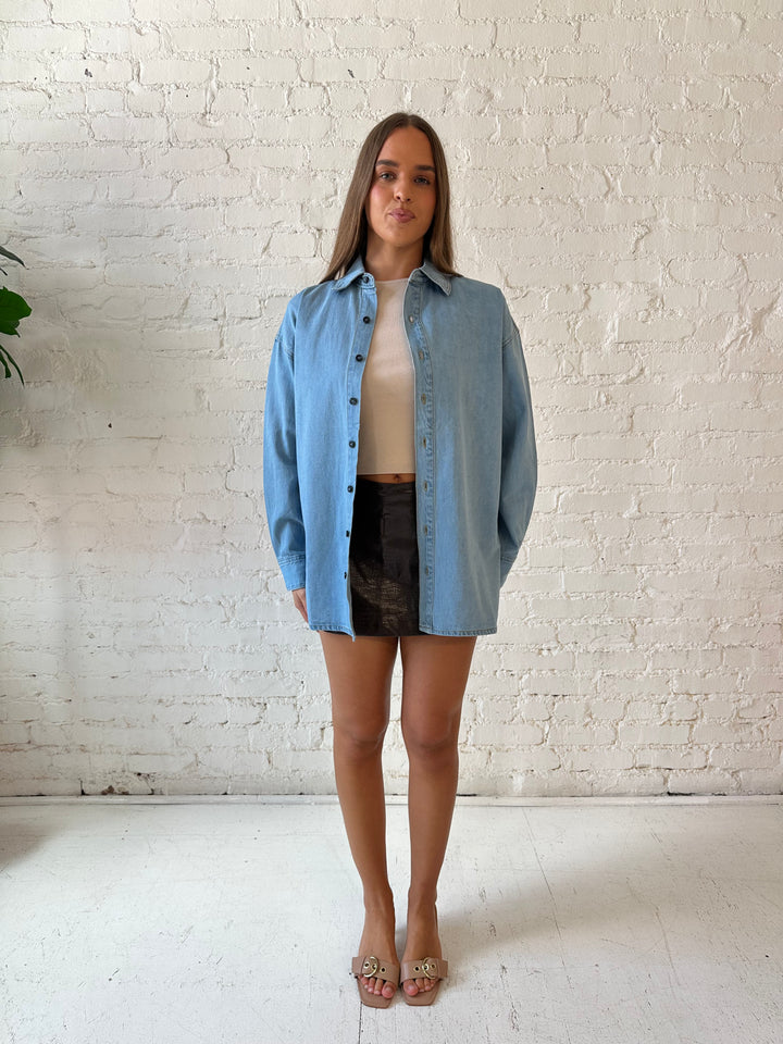 Woman wearing light wash button down denim shirt with leather mini skort. 