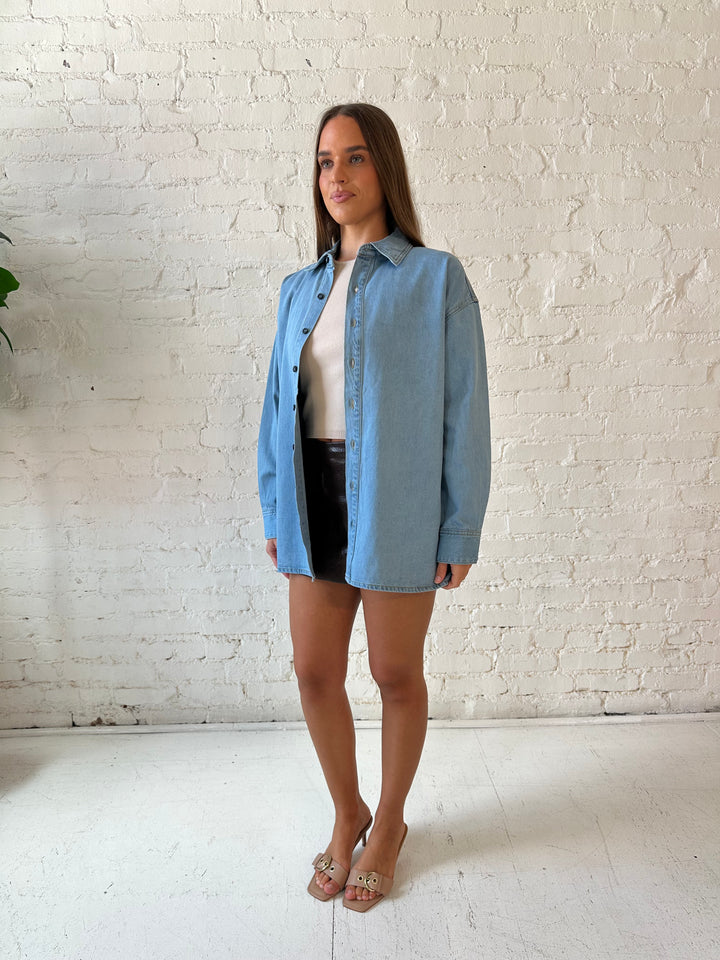 Woman wearing light wash button down denim shirt with leather mini skort. 