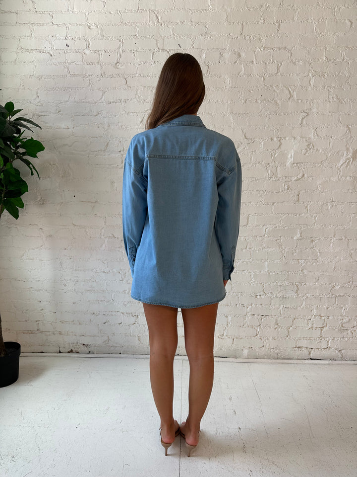 Woman wearing light wash button down denim shirt with leather mini skort. 