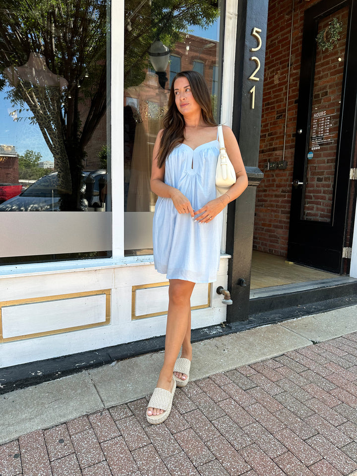 Woman wearing light blue mini dress with keyhole cutout, and adjustable straps. 