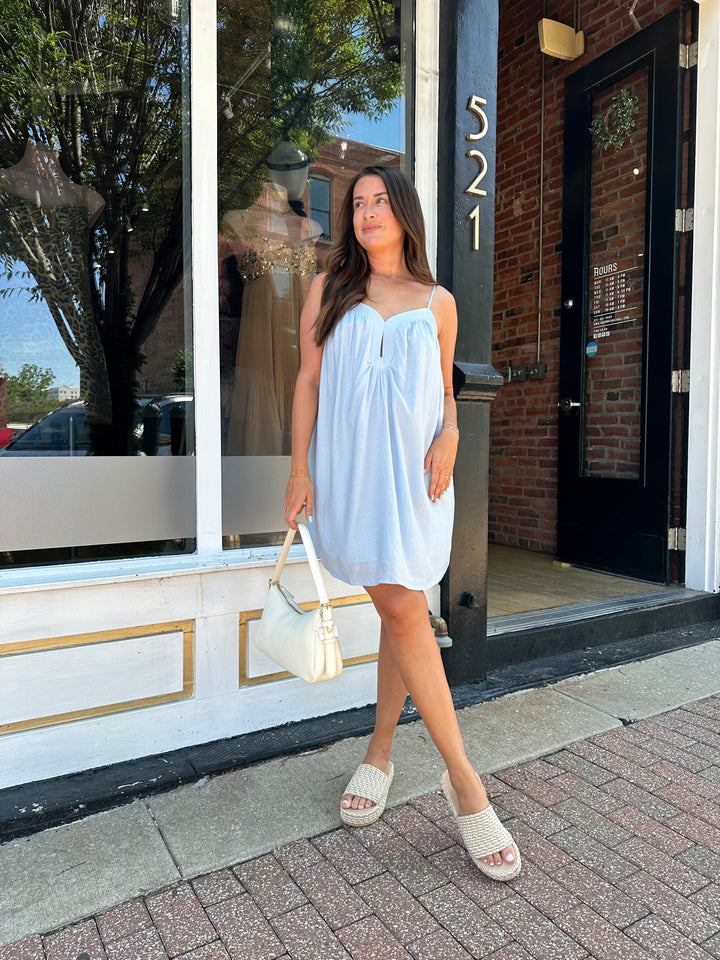 Woman wearing light blue mini dress with keyhole cutout, and adjustable straps. 