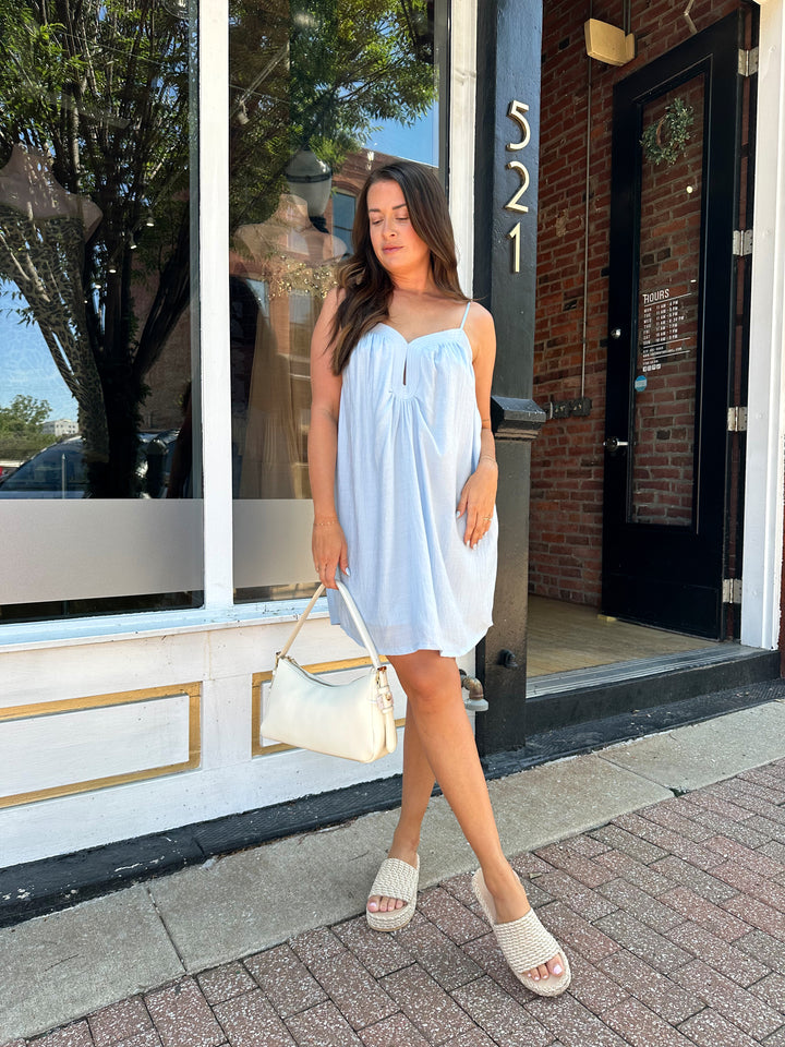 Woman wearing light blue mini dress with keyhole cutout, and adjustable straps. 