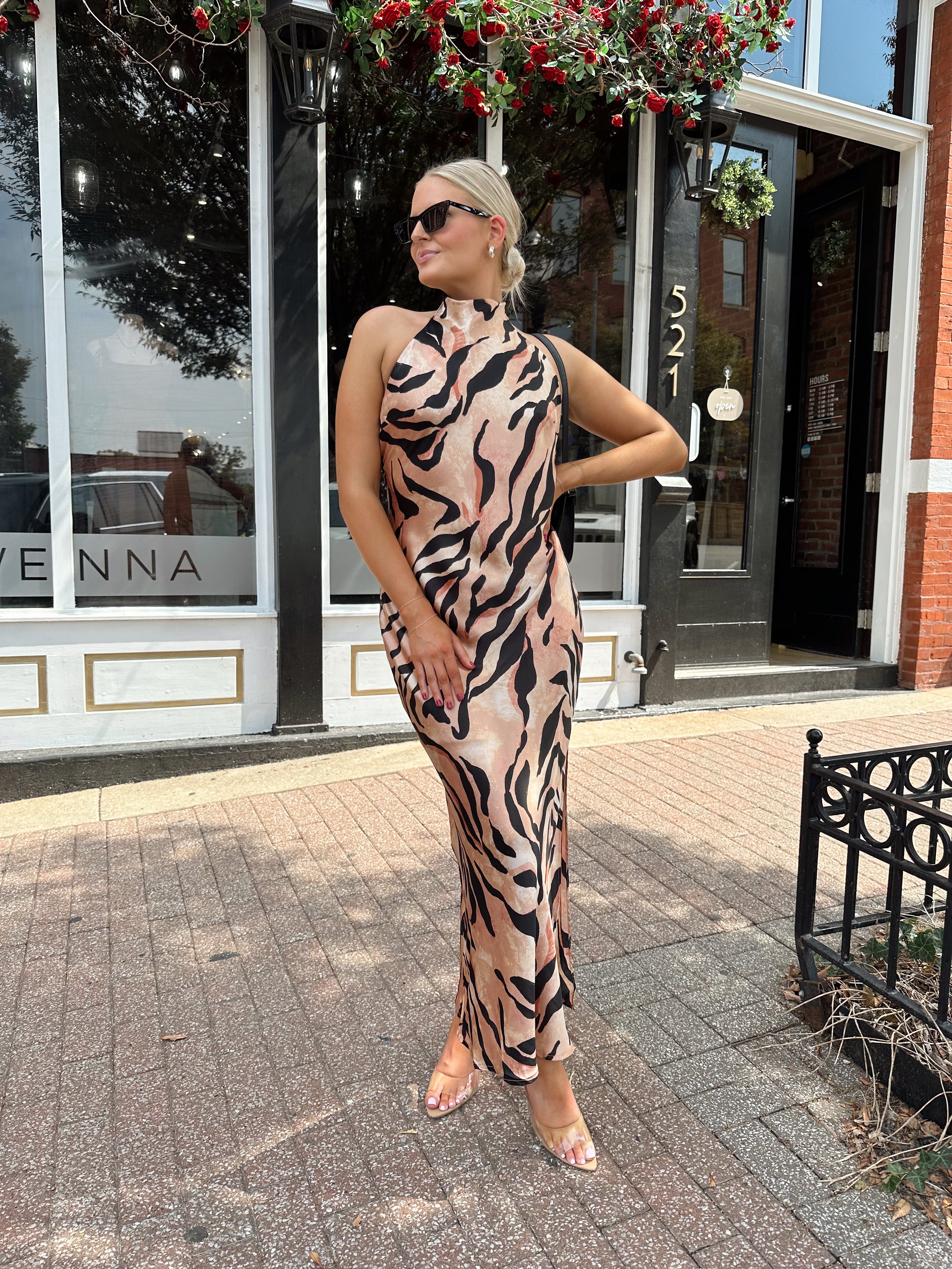 Woman wearing tiger print high neck maxi dress with open back and slit up the side.