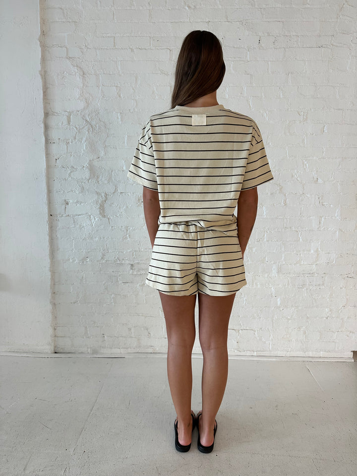 Woman wearing oatmeal and brown striped two piece short lounge set with flip flops. 