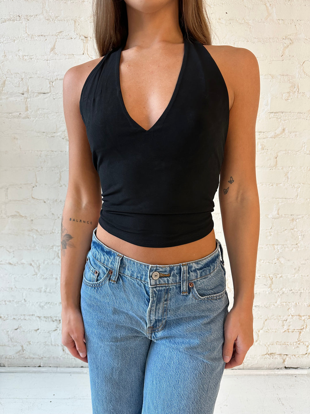 Woman wearing black halter top with open twisted back, and medium wash jeans. 