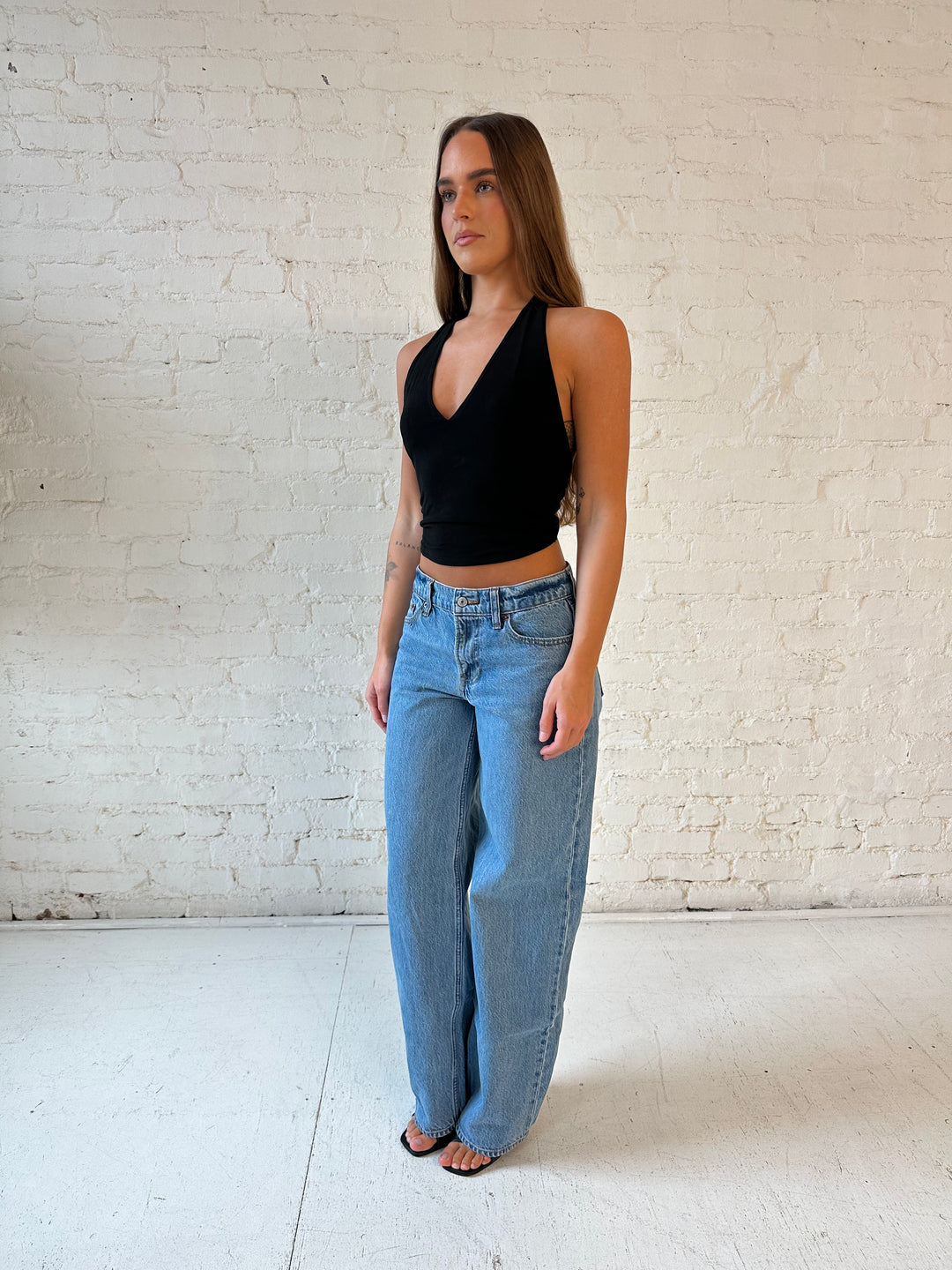 Woman wearing black halter top with open twisted back, and medium wash jeans. 