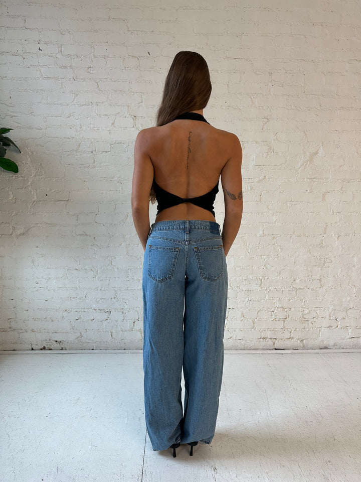 Woman wearing black halter top with open twisted back, and medium wash jeans. 
