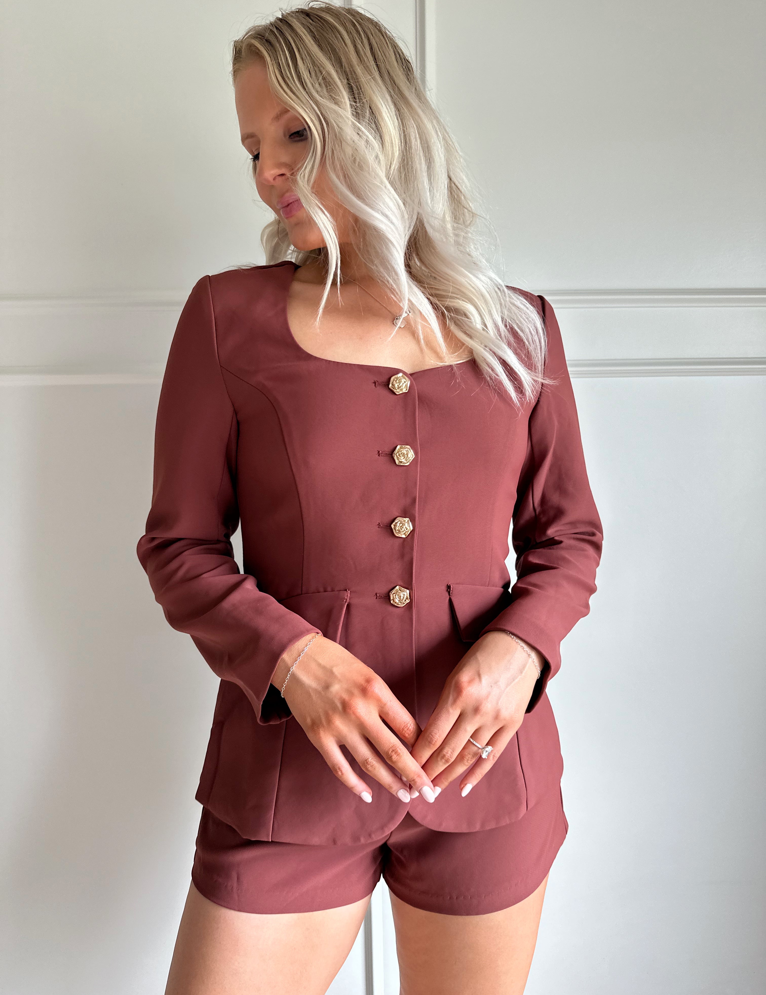 Woman wearing a dark rose colored tailored romper with long sleeves, and button closure. 