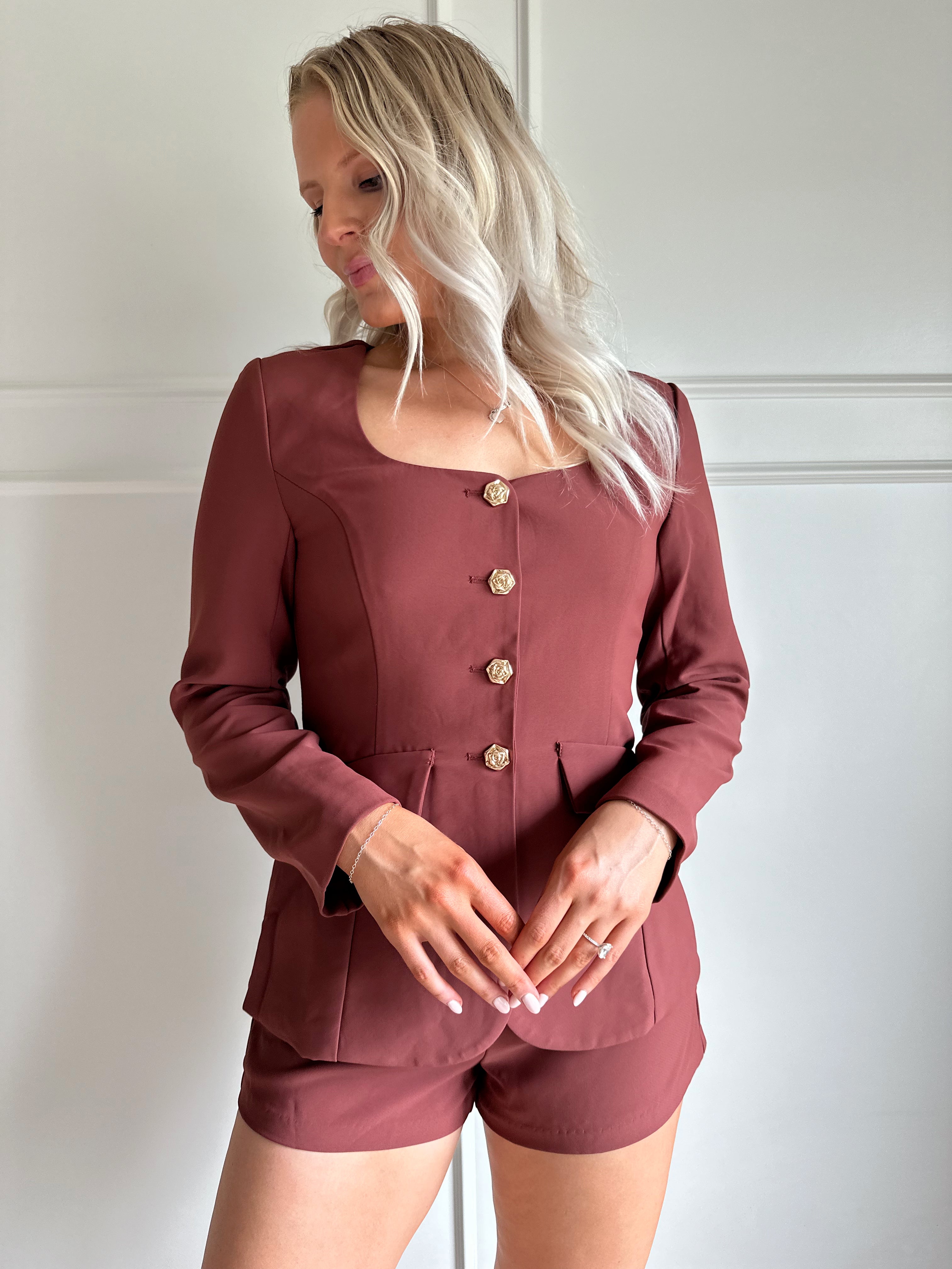 Woman wearing a dark rose colored tailored romper with long sleeves, and button closure. 