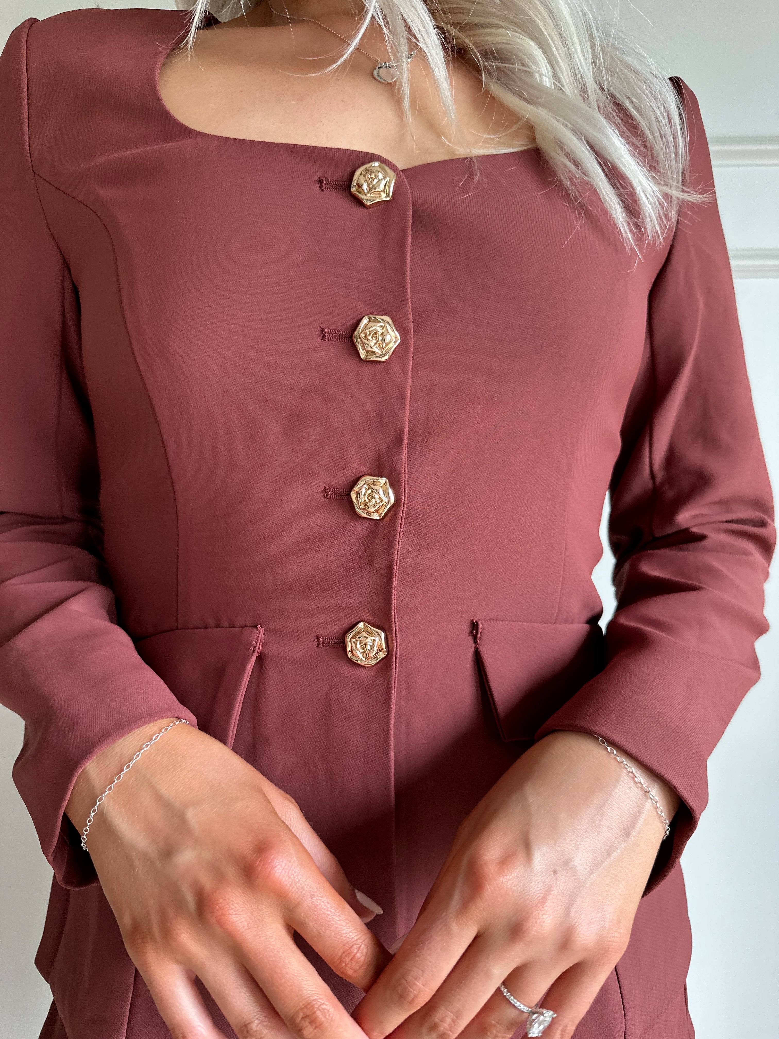 Woman wearing a dark rose colored tailored romper with long sleeves, and button closure. 