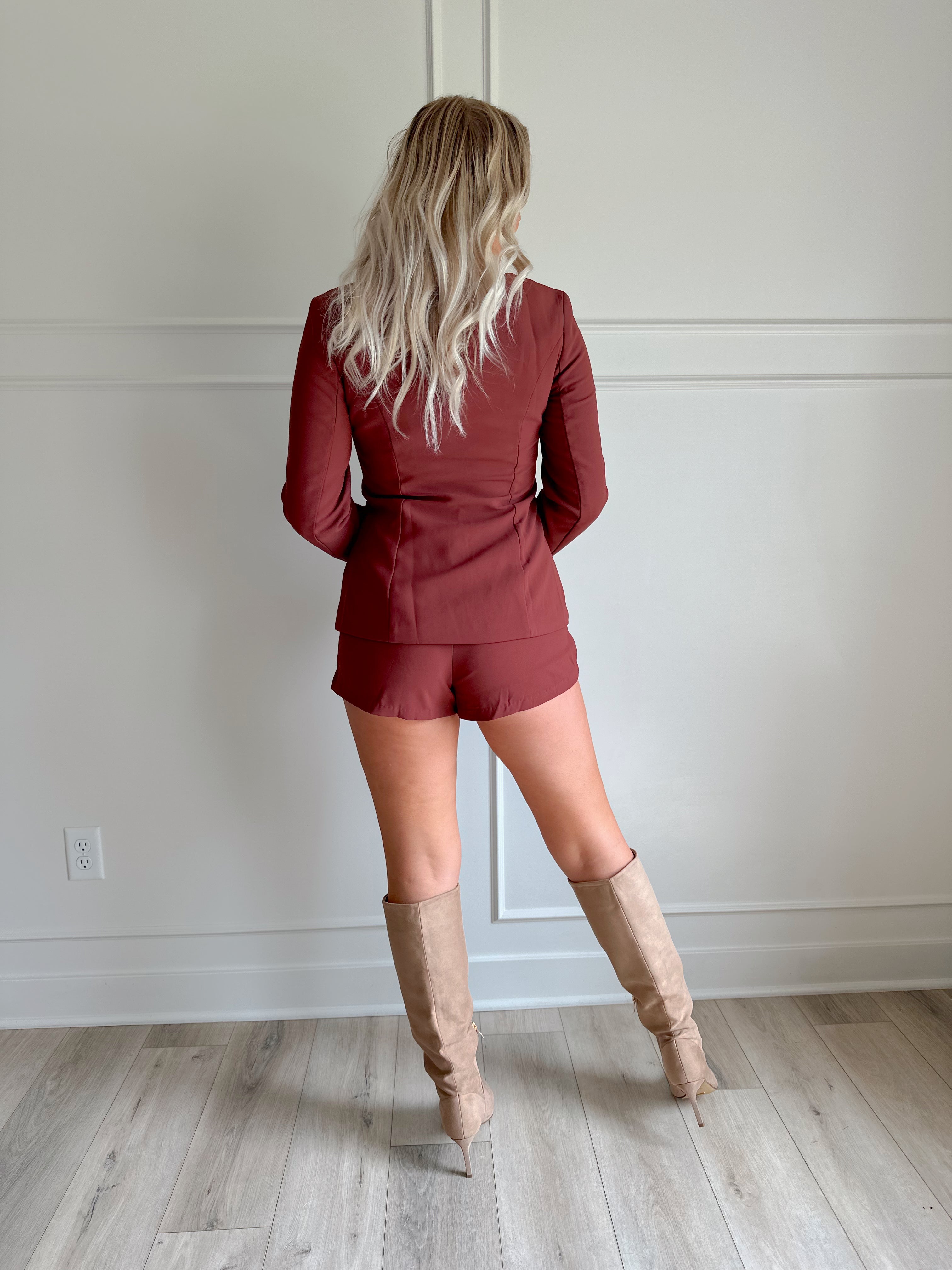 Woman wearing a dark rose colored tailored romper with long sleeves, and button closure. 