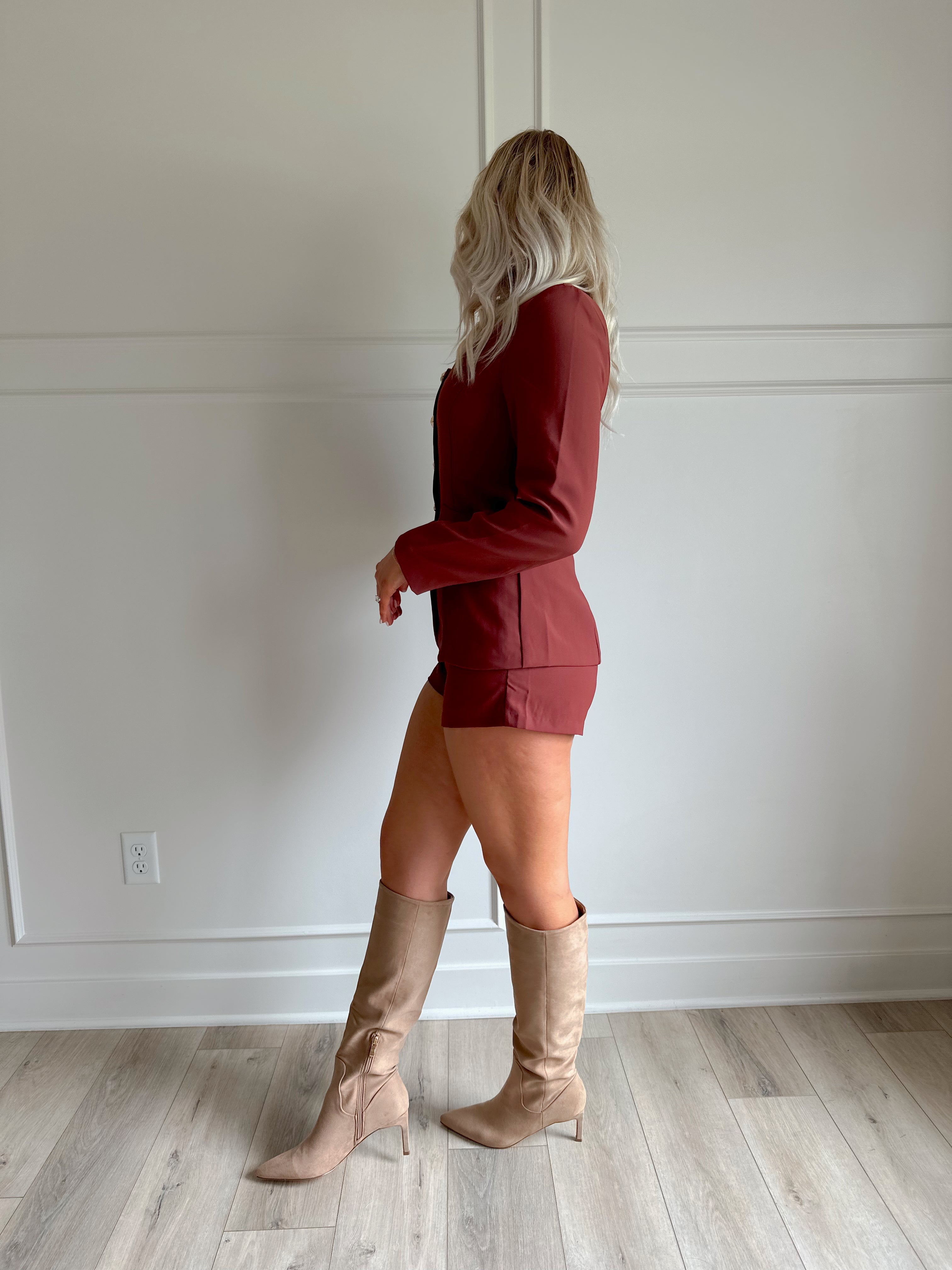 Woman wearing a dark rose colored tailored romper with long sleeves, and button closure. 