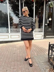 Woman wearing black and white striped long sleeve sweater dress with black chunky heel.