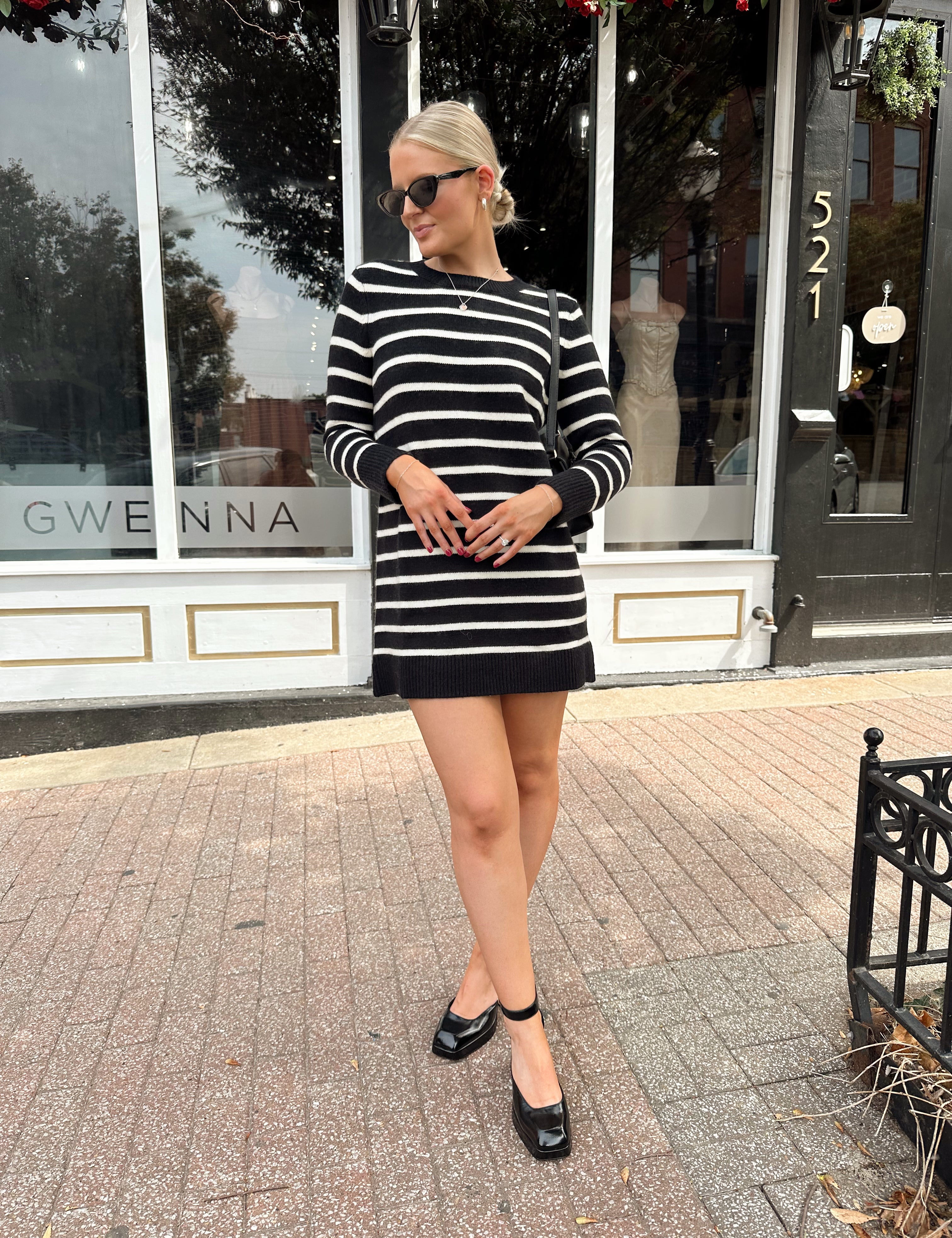 Woman wearing black and white striped long sleeve sweater dress with black chunky heel.
