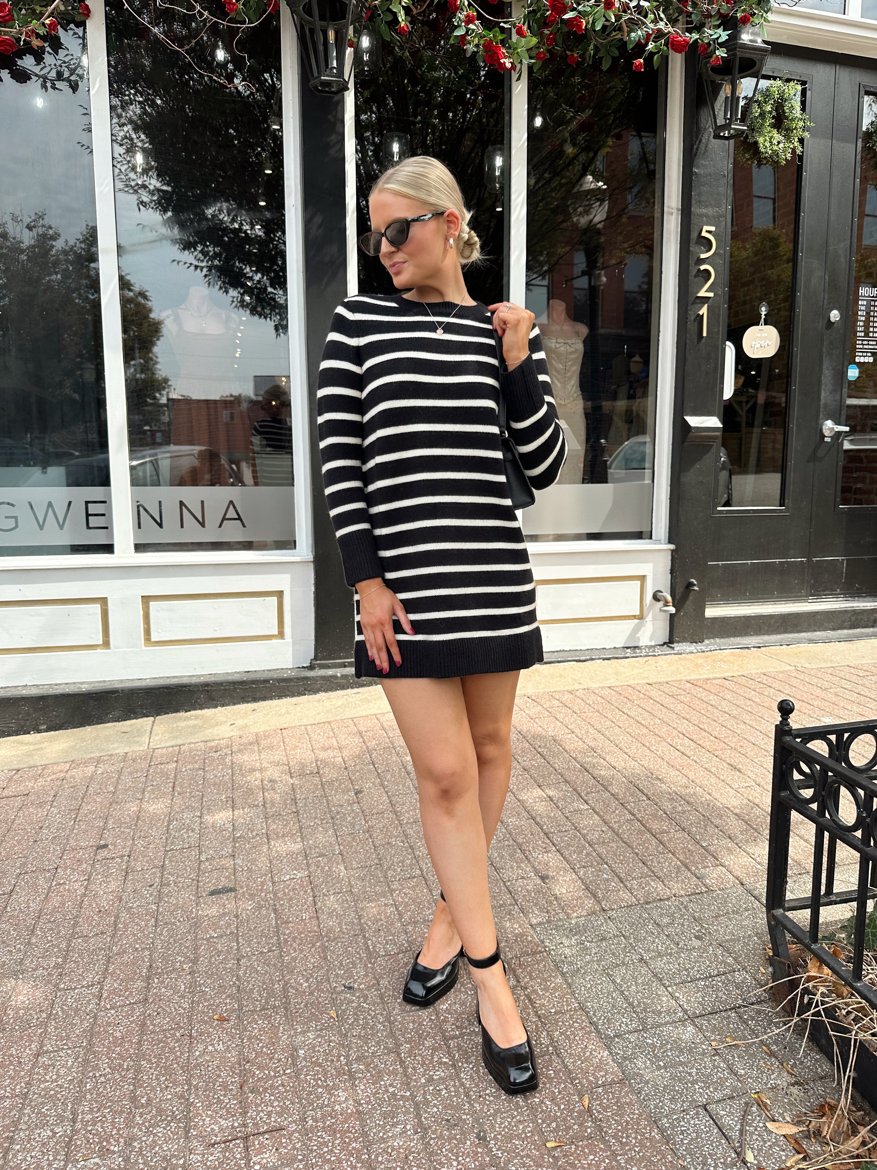 Woman wearing black and white striped long sleeve sweater dress with black chunky heel.
