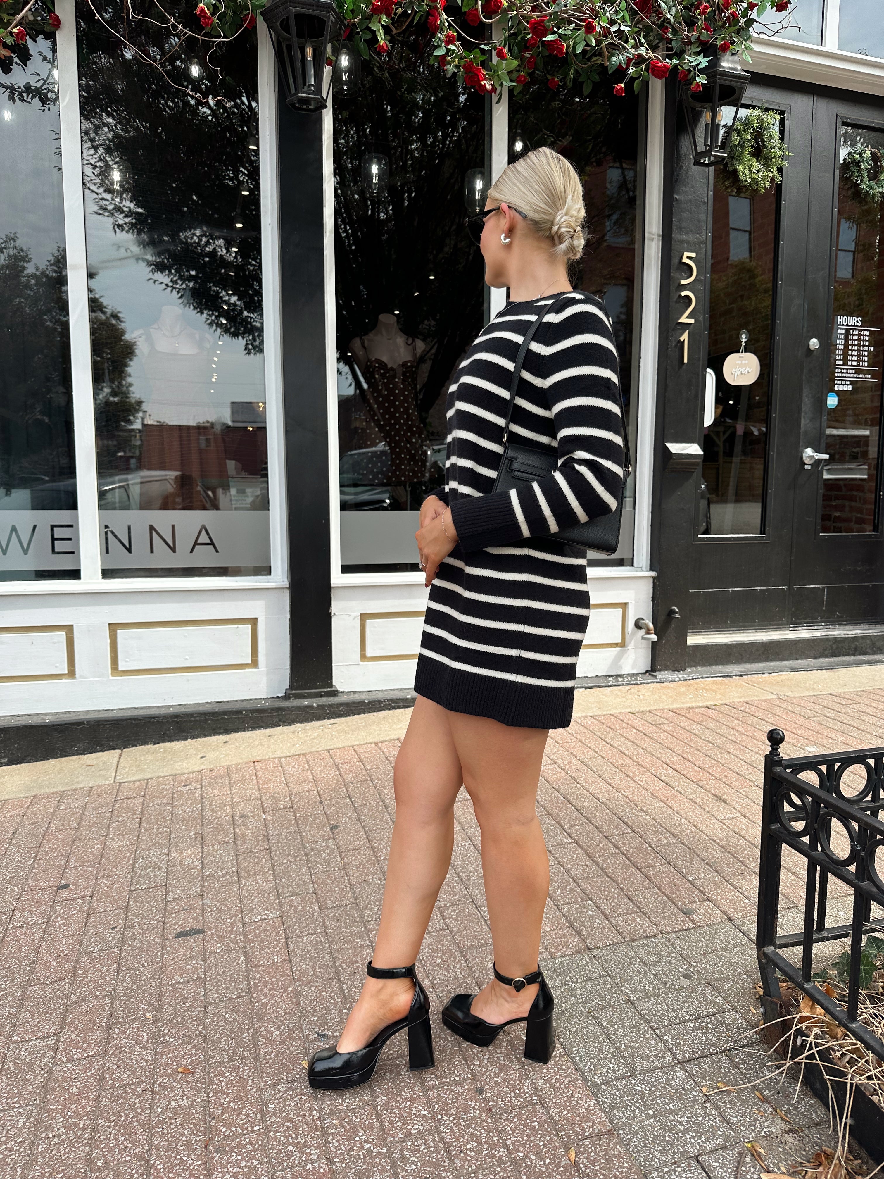 Woman wearing black and white striped long sleeve sweater dress with black chunky heel.