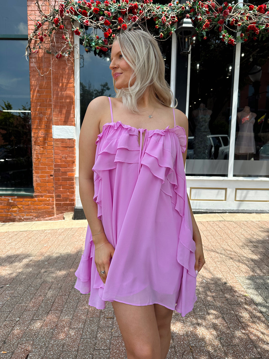 Woman wearing pink ruffle mini dress with adjustable straps, and tiered detailing. 