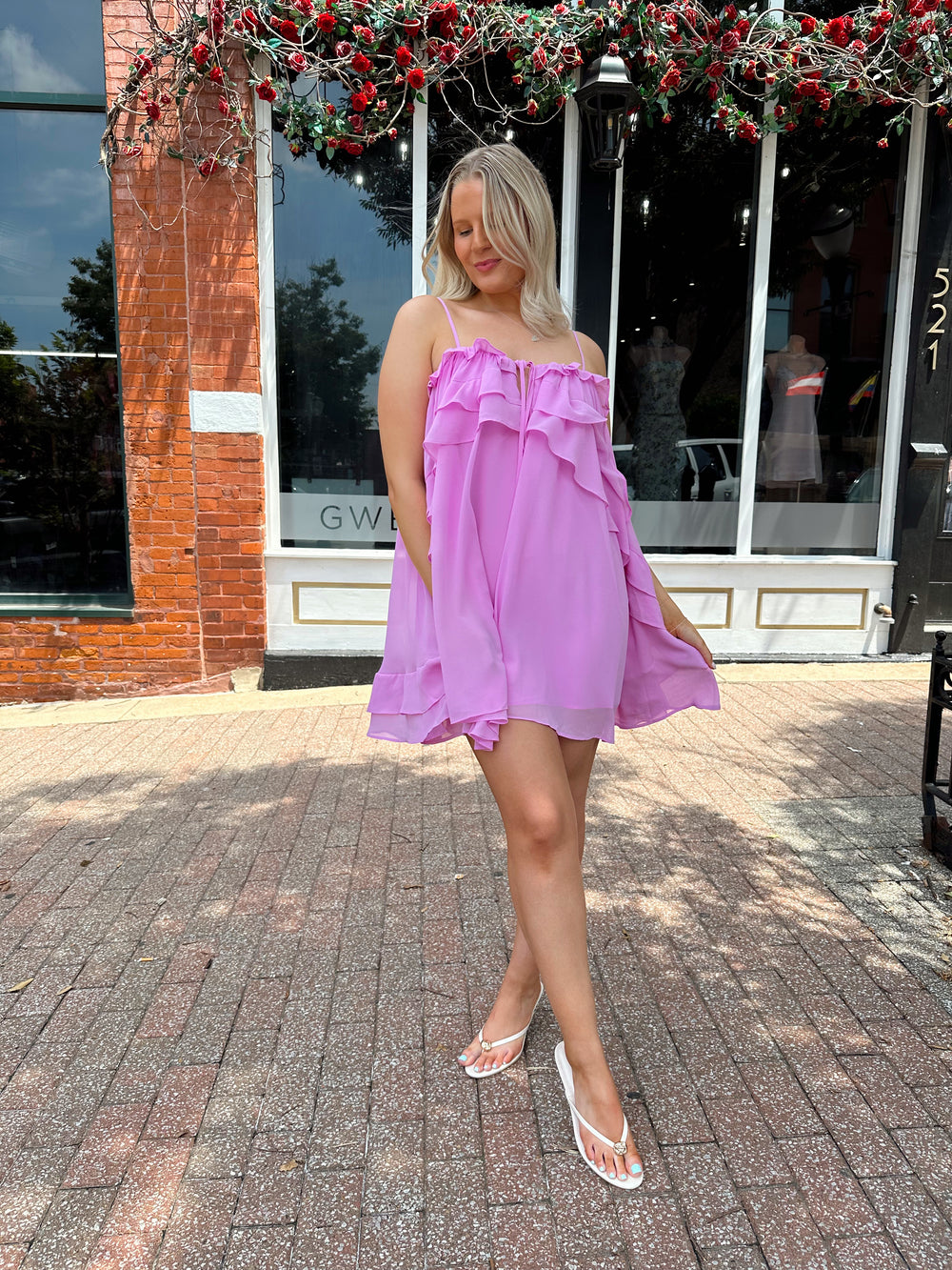 Woman wearing pink ruffle mini dress with adjustable straps, and tiered detailing. 