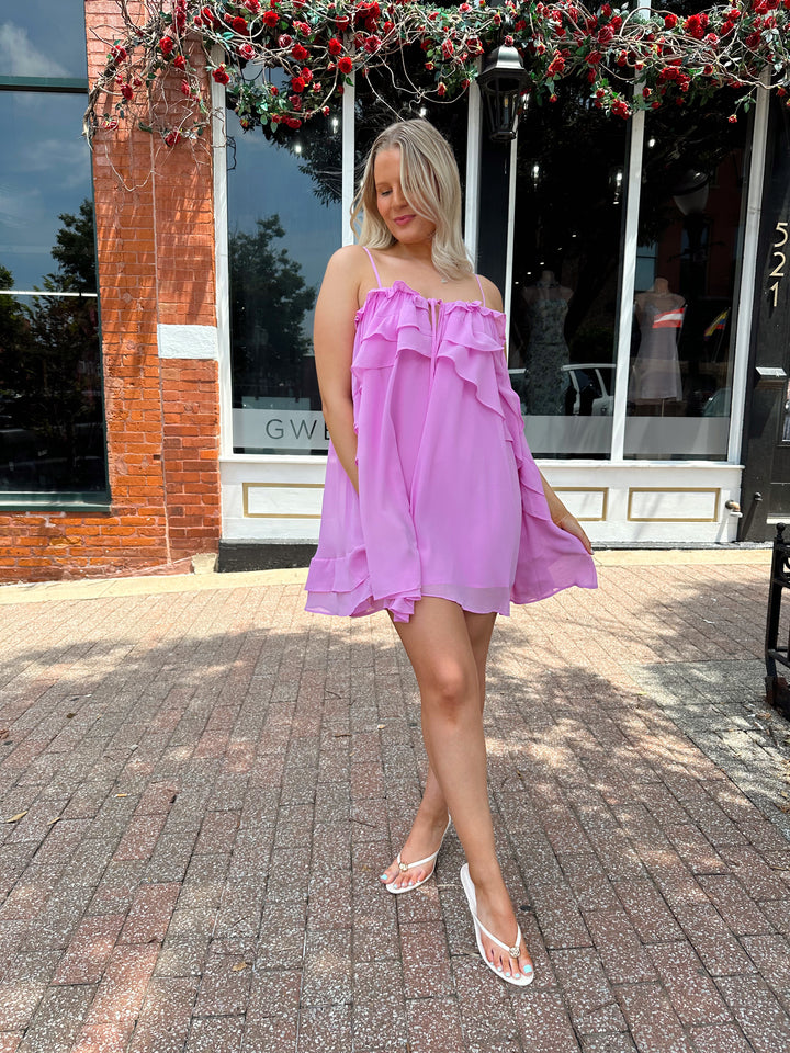 Woman wearing pink ruffle mini dress with adjustable straps, and tiered detailing. 