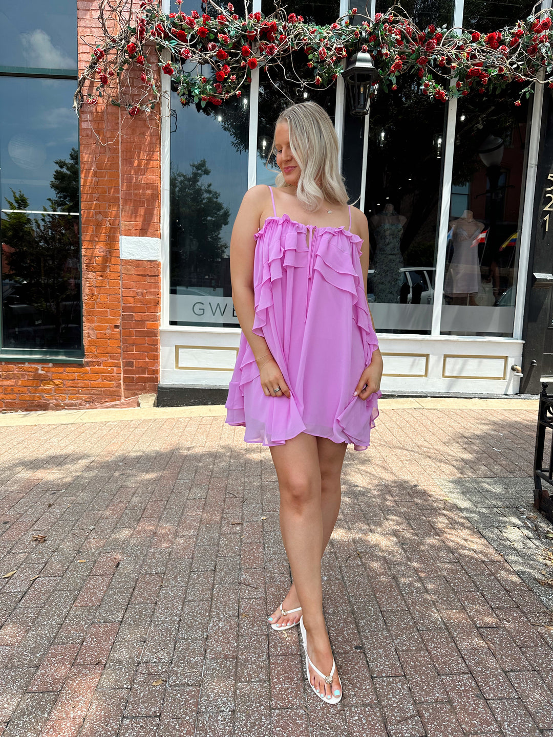 Woman wearing pink ruffle mini dress with adjustable straps, and tiered detailing. 