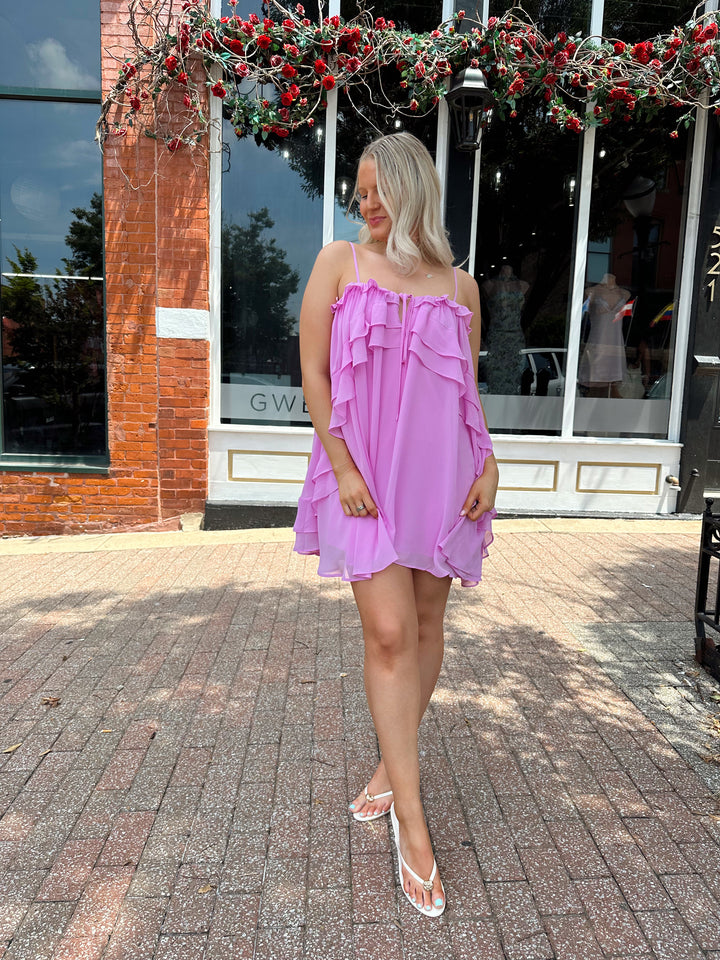 Woman wearing pink ruffle mini dress with adjustable straps, and tiered detailing. 