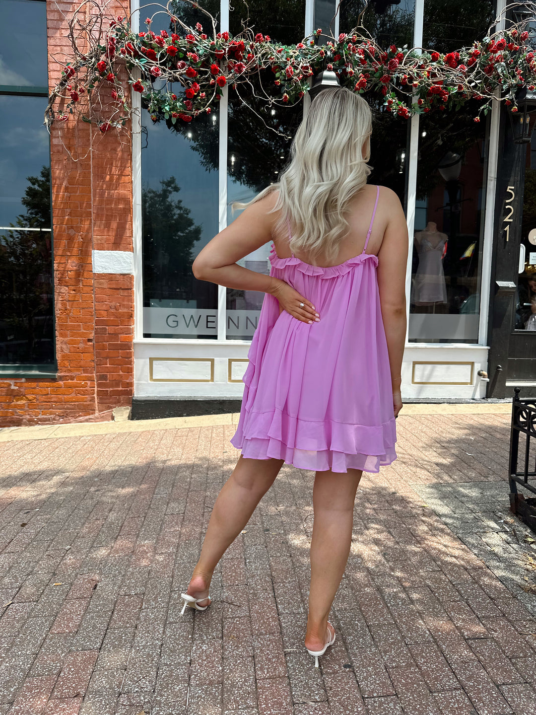 Woman wearing pink ruffle mini dress with adjustable straps, and tiered detailing. 
