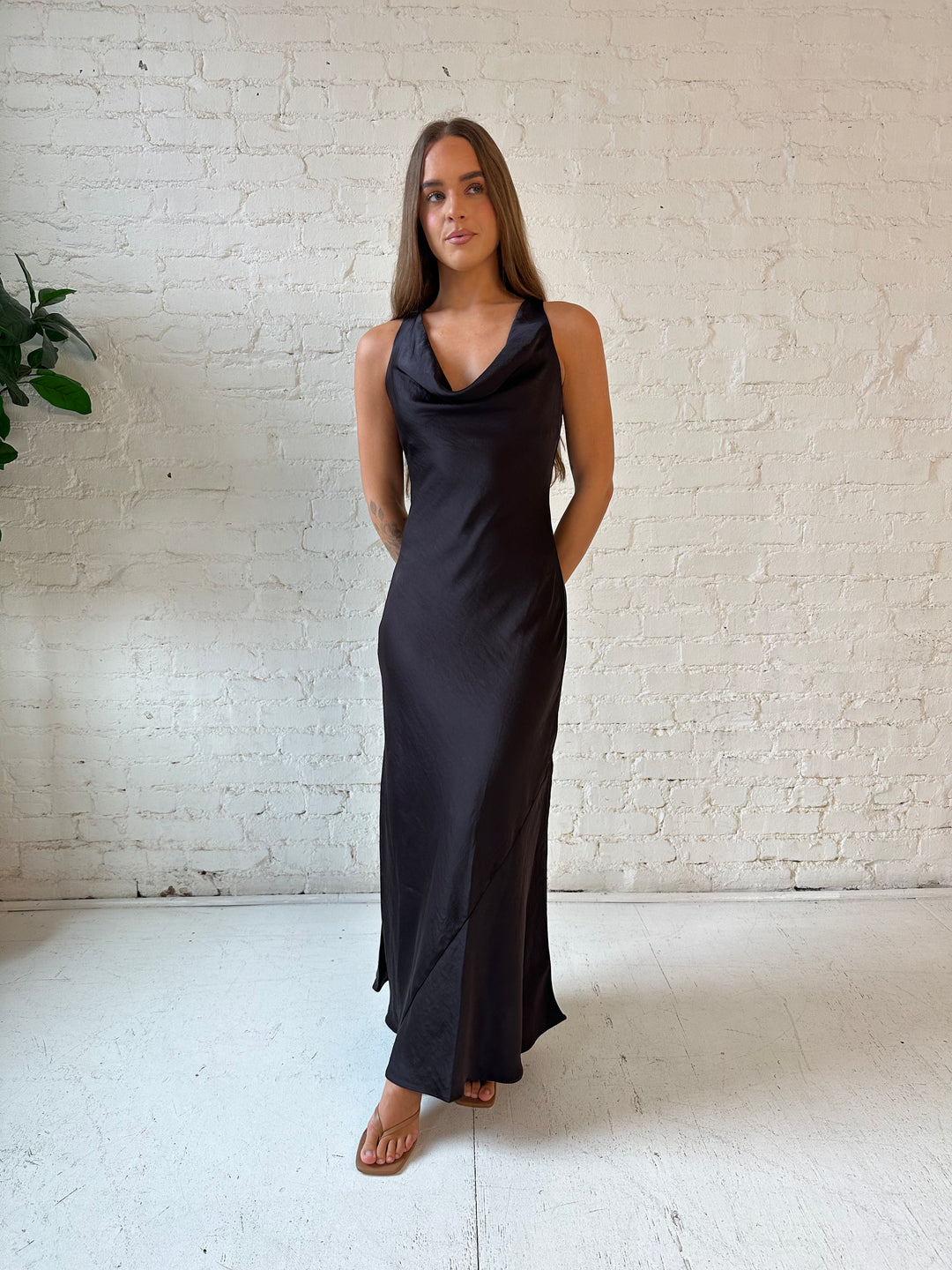 Woman wearing dark brown satin maxi dress with high cowl neckline, and cowl back with tie. 