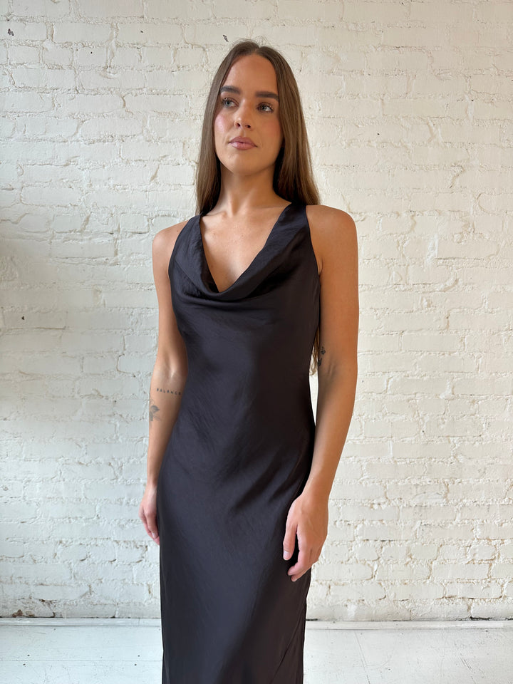 Woman wearing dark brown satin maxi dress with high cowl neckline, and cowl back with tie. 