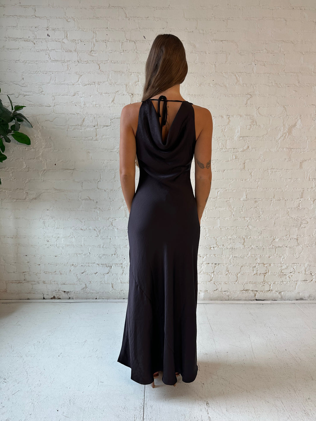Woman wearing dark brown satin maxi dress with high cowl neckline, and cowl back with tie. 