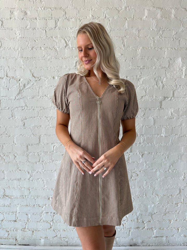 Woman wearing brown striped denim mini dress with zipper front closure and puff sleeves.