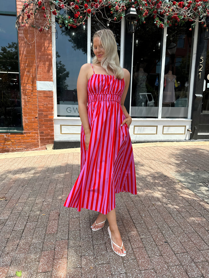 Woman wearing pink and red striped midi dress with cinched waist, and adjustable straps.