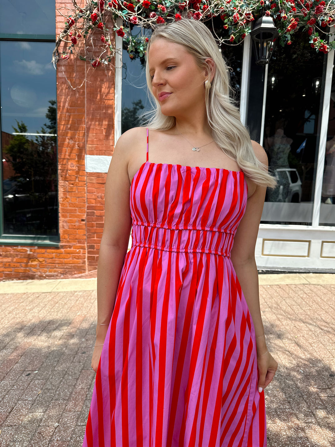 Woman wearing pink and red striped midi dress with cinched waist, and adjustable straps.