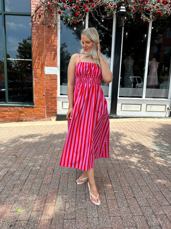 Woman wearing pink and red striped midi dress with cinched waist, and adjustable straps.