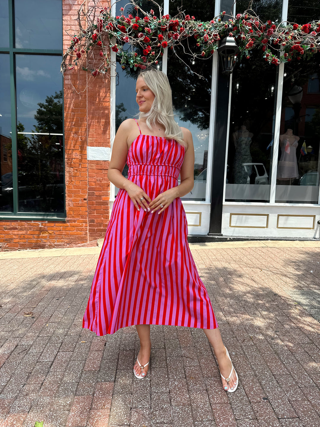 Woman wearing pink and red striped midi dress with cinched waist, and adjustable straps.