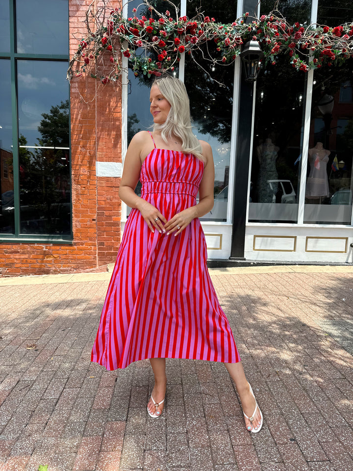 Woman wearing pink and red striped midi dress with cinched waist, and adjustable straps.