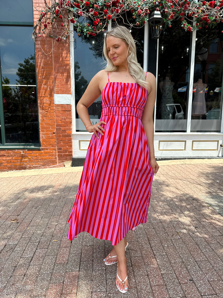 Woman wearing pink and red striped midi dress with cinched waist, and adjustable straps.