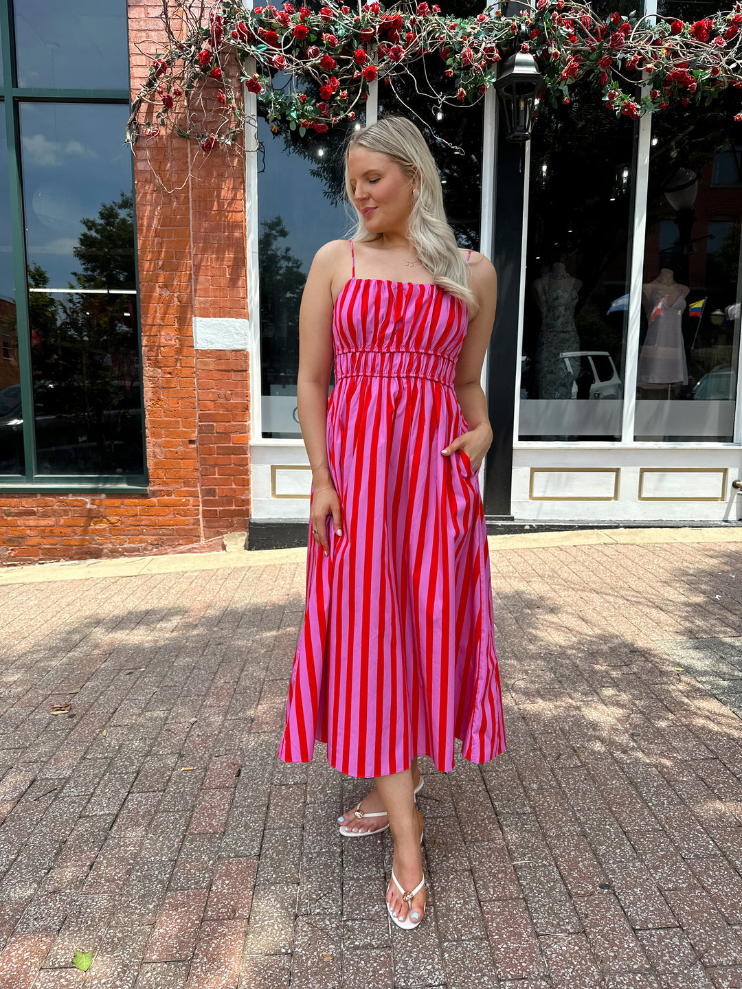 Woman wearing pink and red striped midi dress with cinched waist, and adjustable straps.