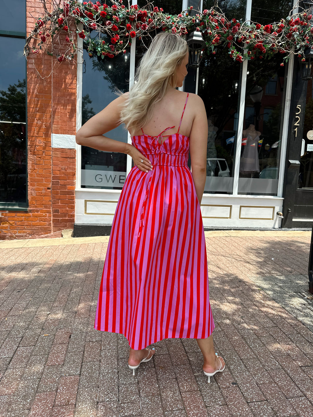 Woman wearing pink and red striped midi dress with cinched waist, and adjustable straps.