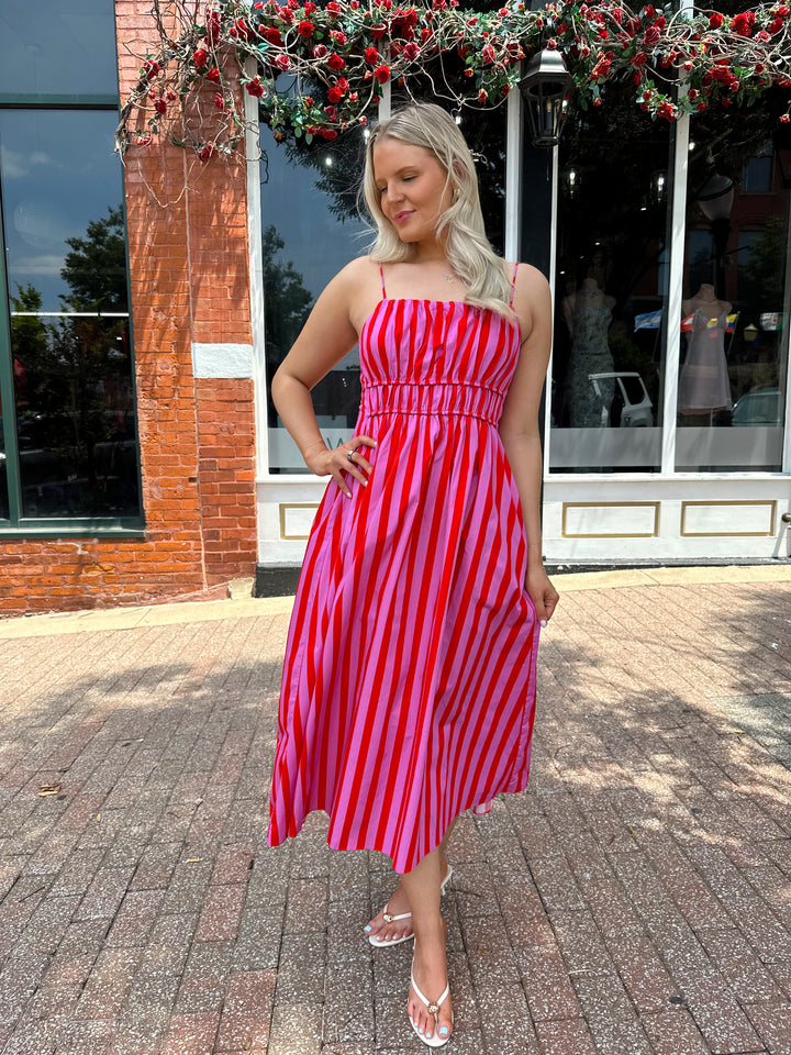 Woman wearing pink and red striped midi dress with cinched waist, and adjustable straps.