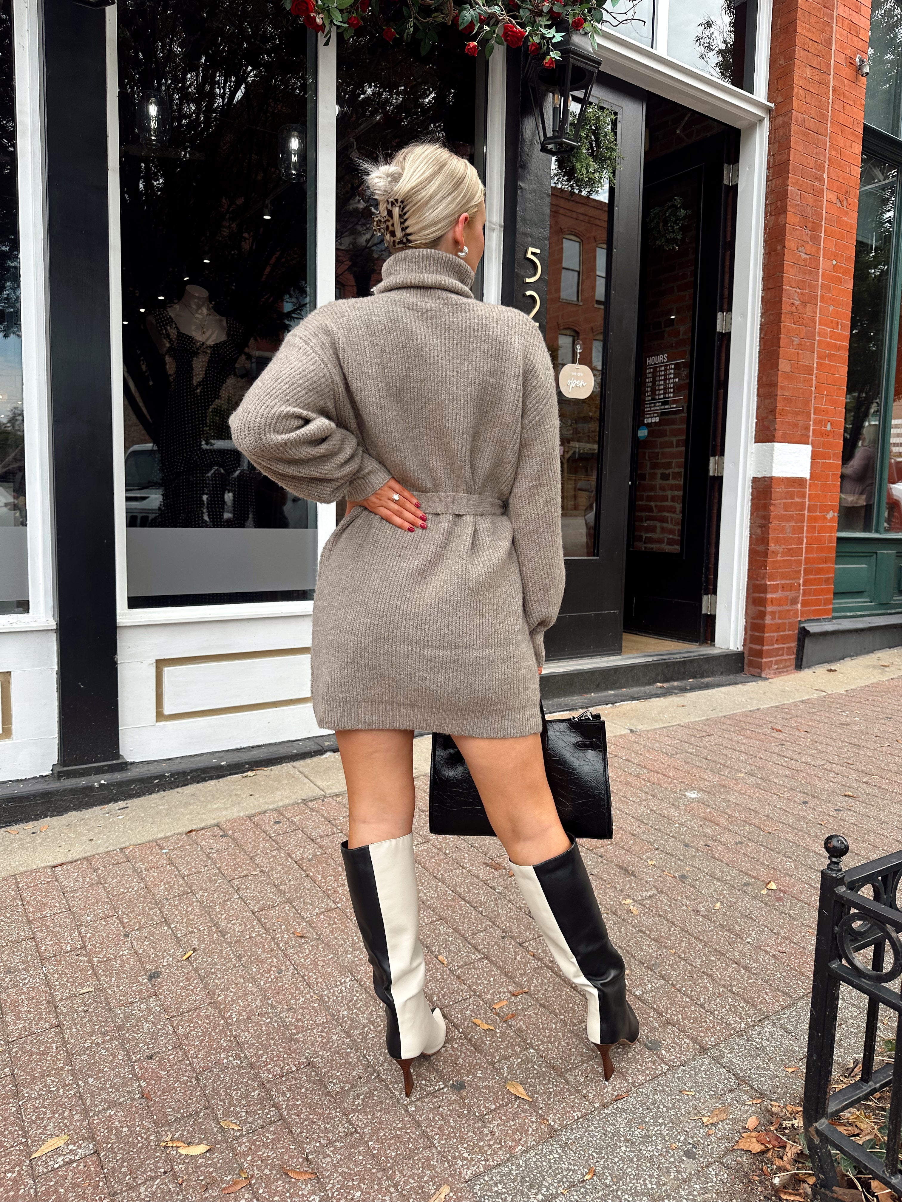 Woman wearing taupe turtle neck sweater dress with belt detail.