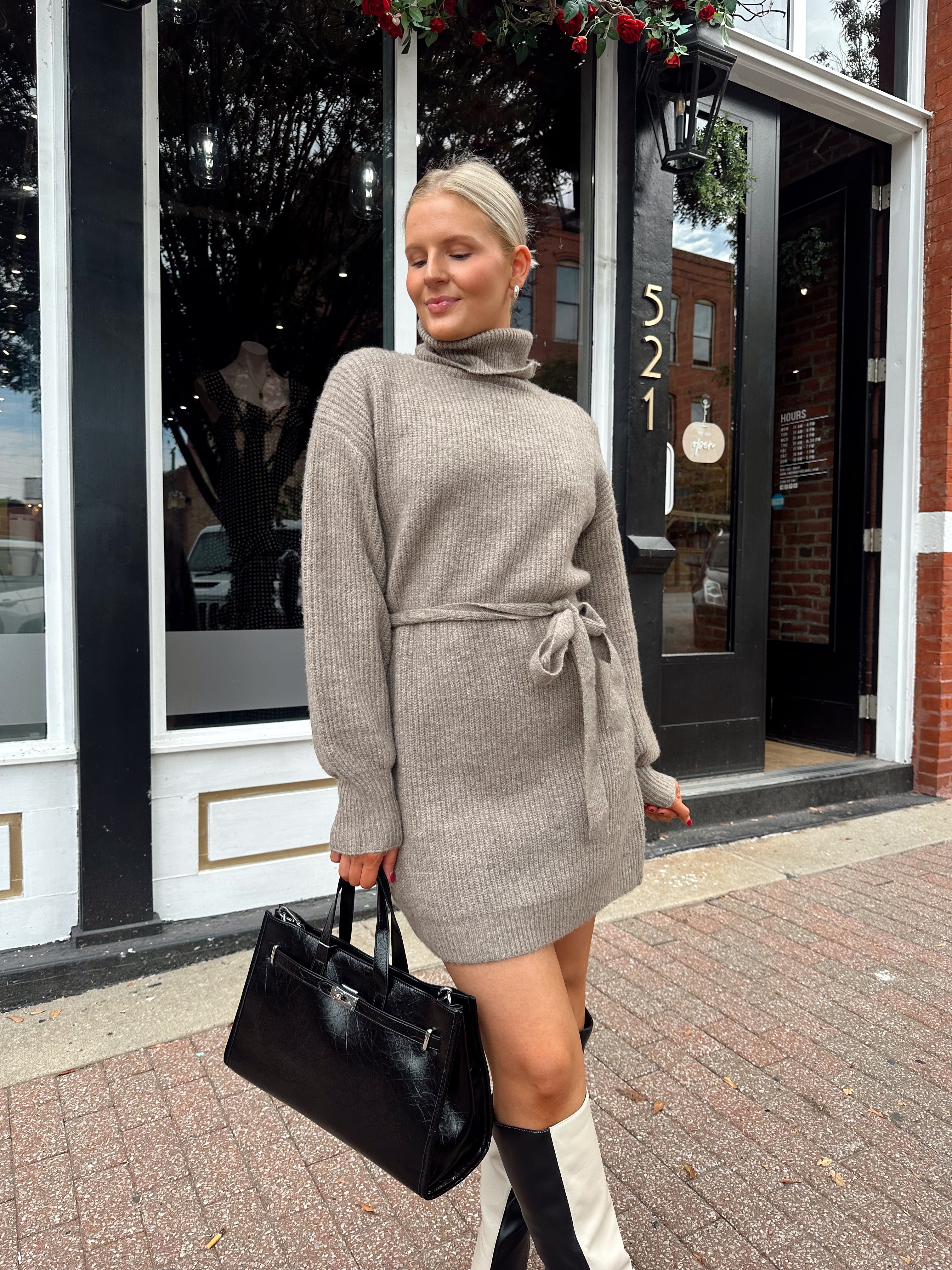 Woman wearing taupe turtle neck sweater dress with belt detail.