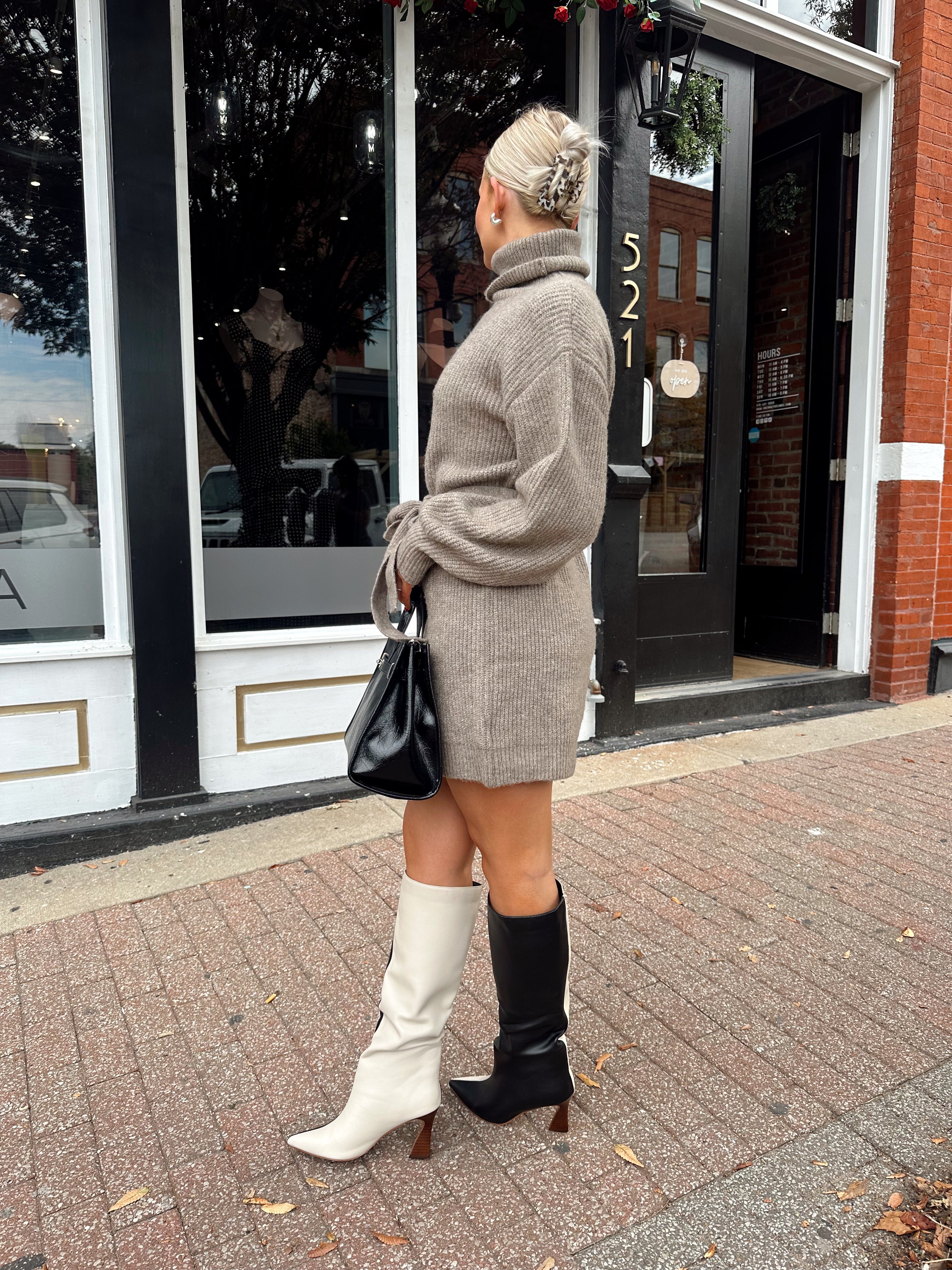 Woman wearing taupe turtle neck sweater dress with belt detail.