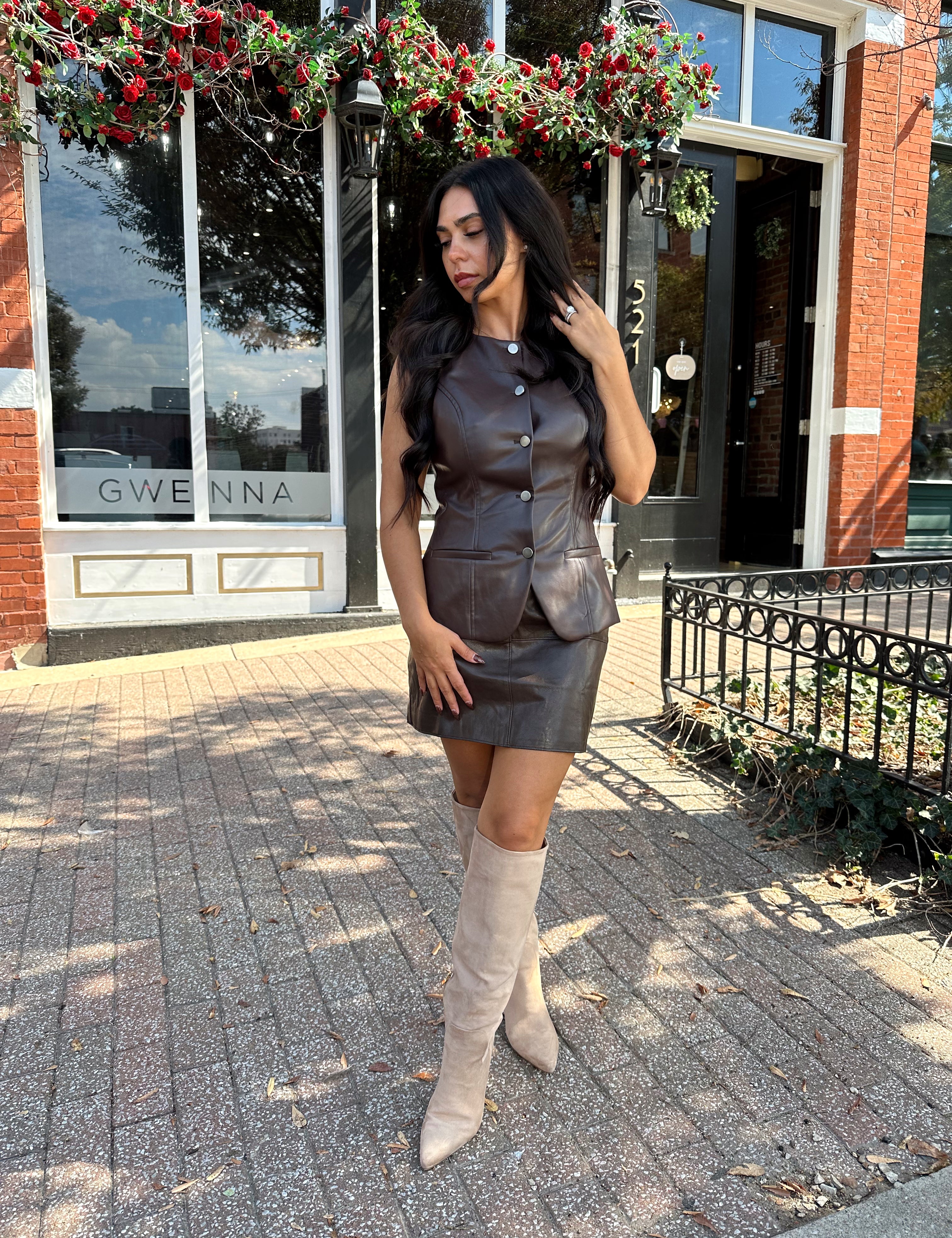 Woman wearing dark brown leather button up vest with matching skirt. 