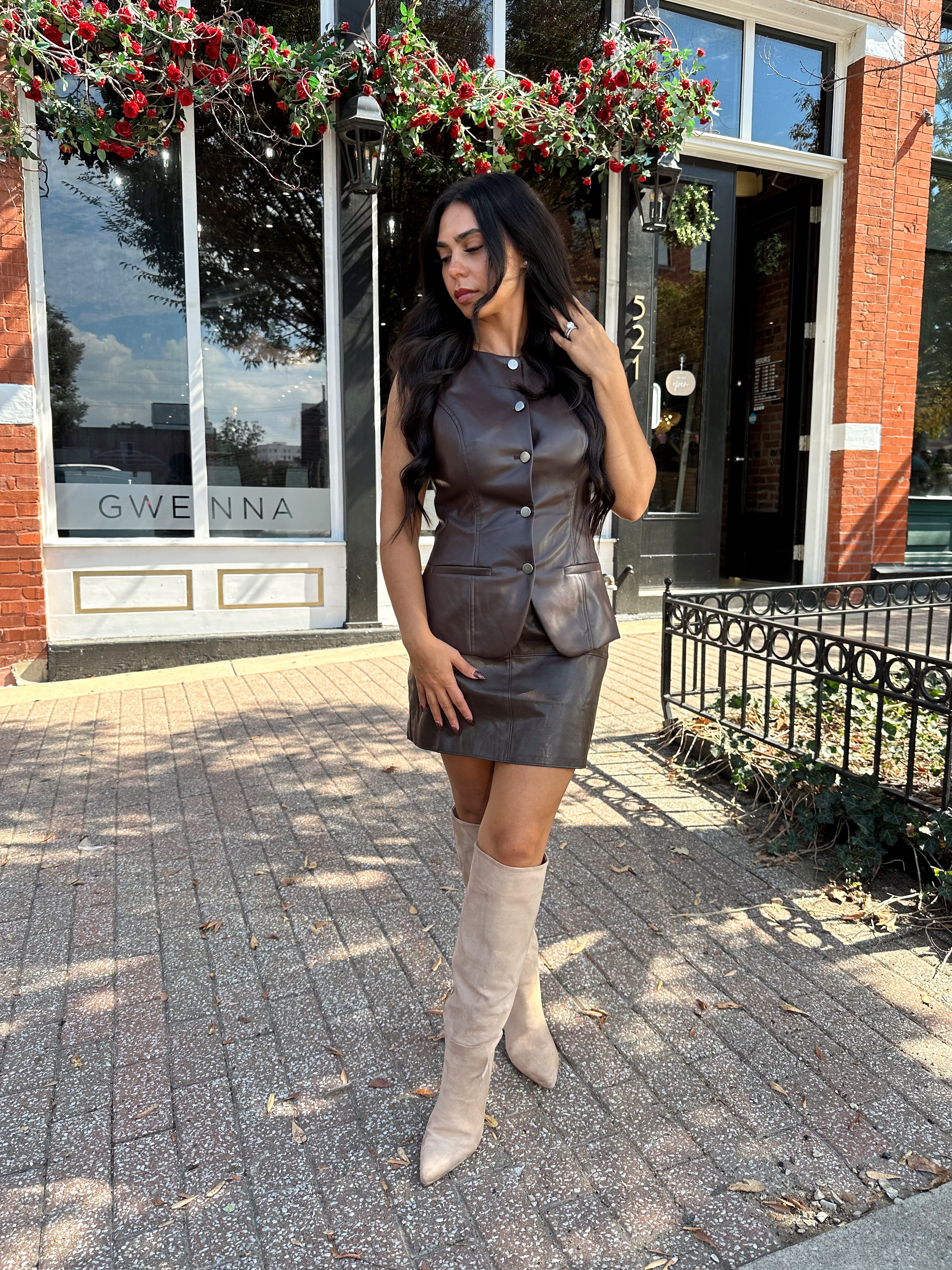 Woman wearing dark brown leather button up vest with matching skirt. 