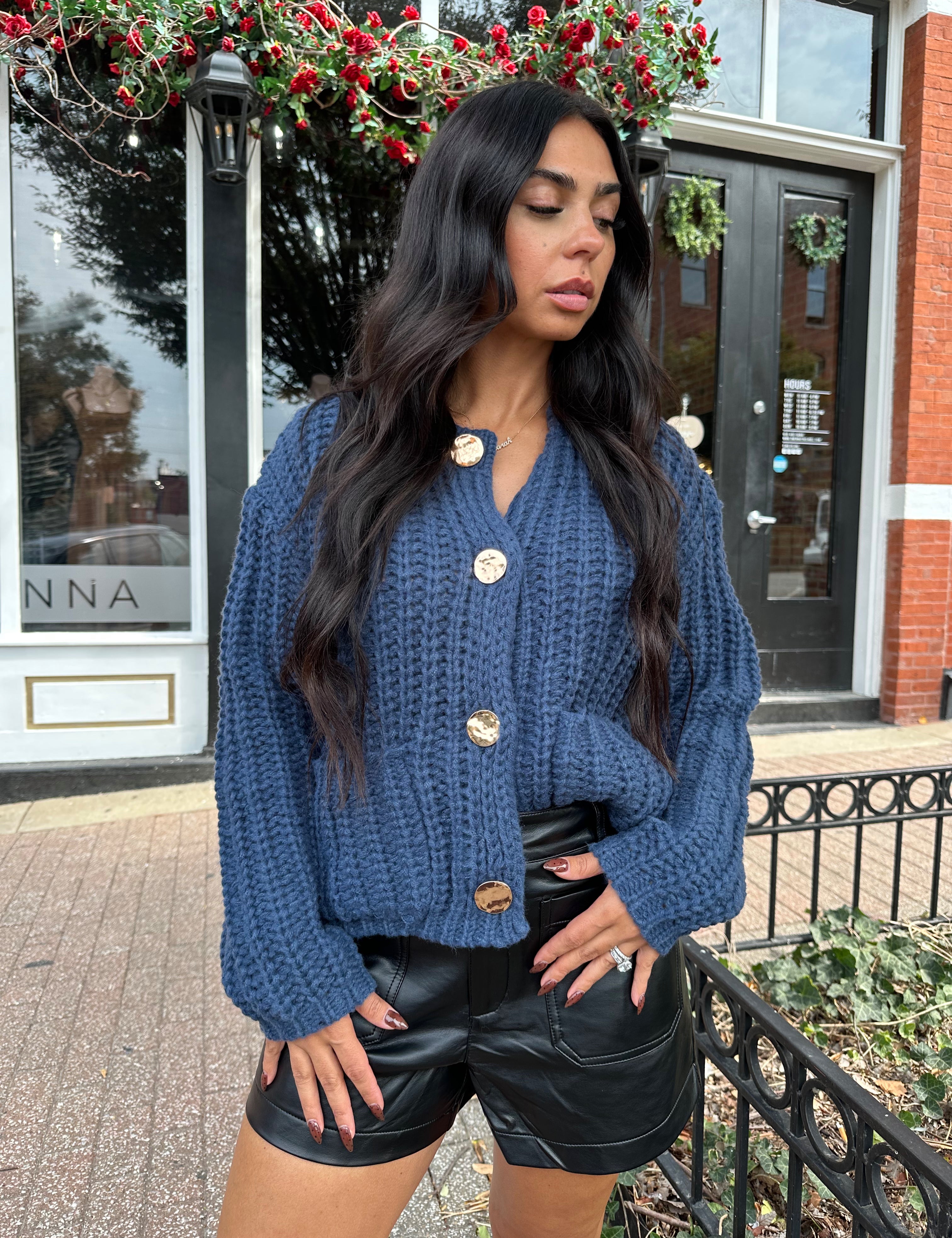 Woman wearing dark blue chunky cardigan with gold button closure. 