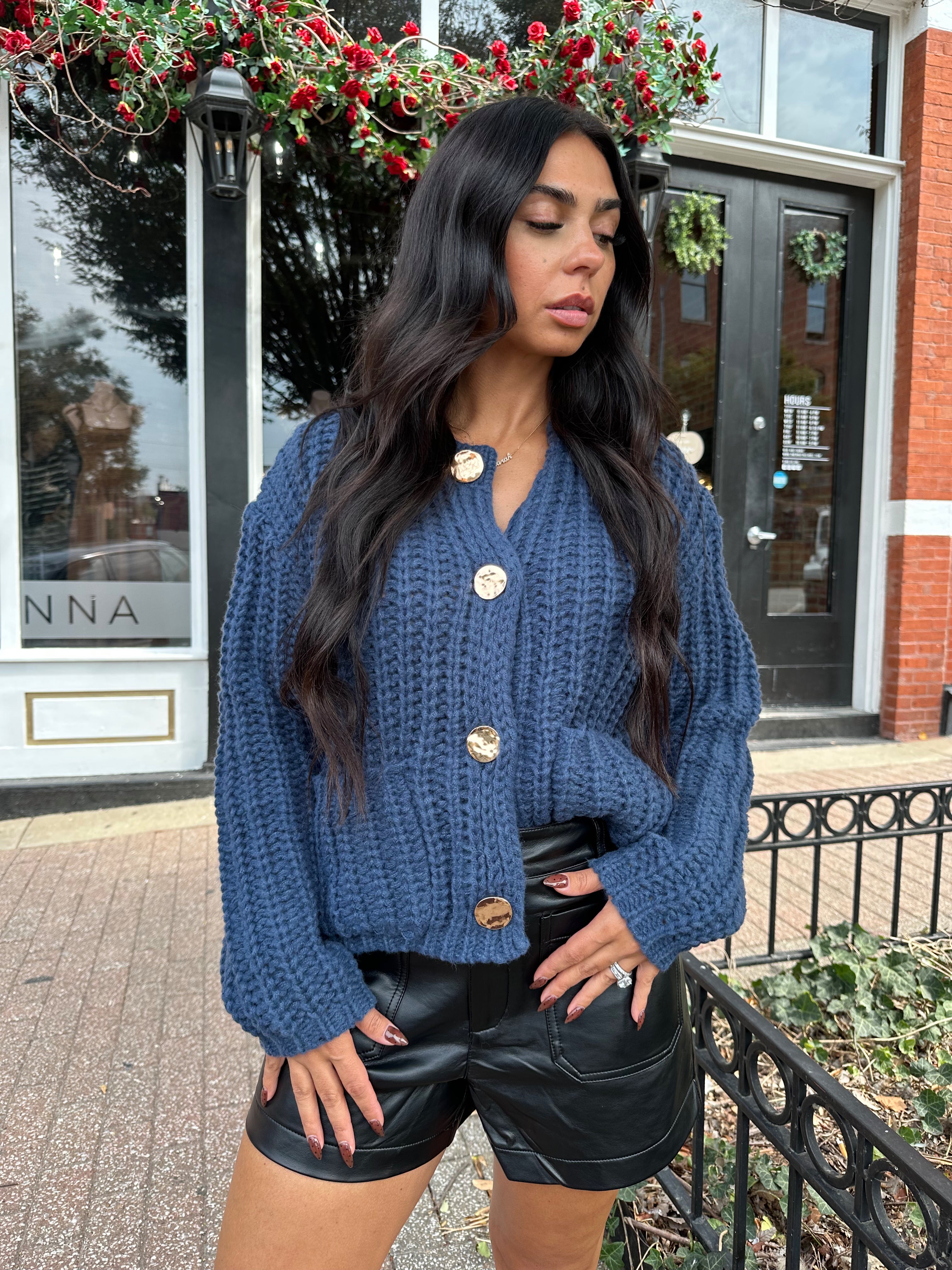 Woman wearing dark blue chunky cardigan with gold button closure. 