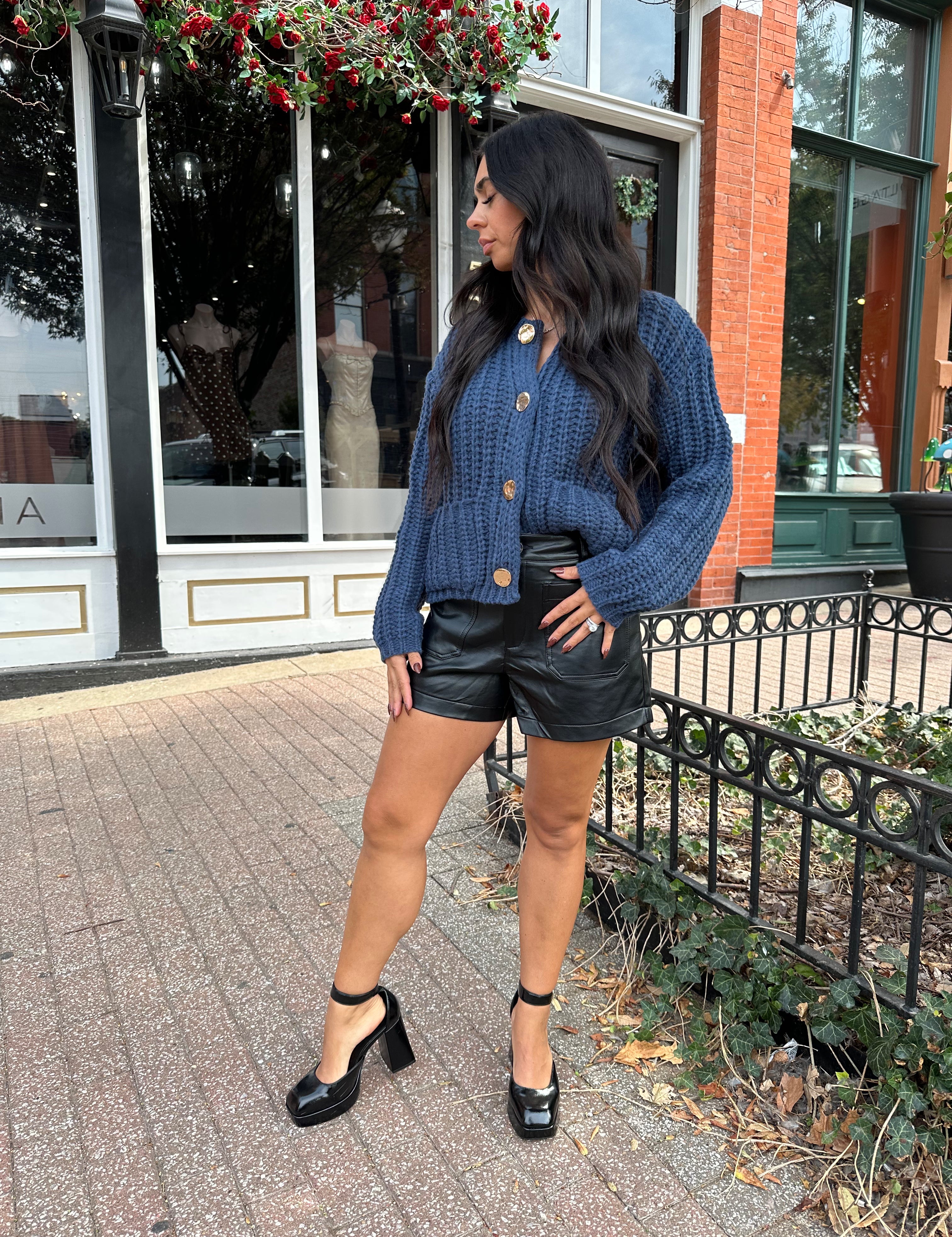 Woman wearing dark blue chunky cardigan with gold button closure. 