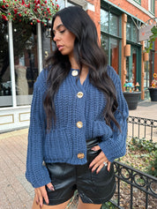 Woman wearing dark blue chunky cardigan with gold button closure. 